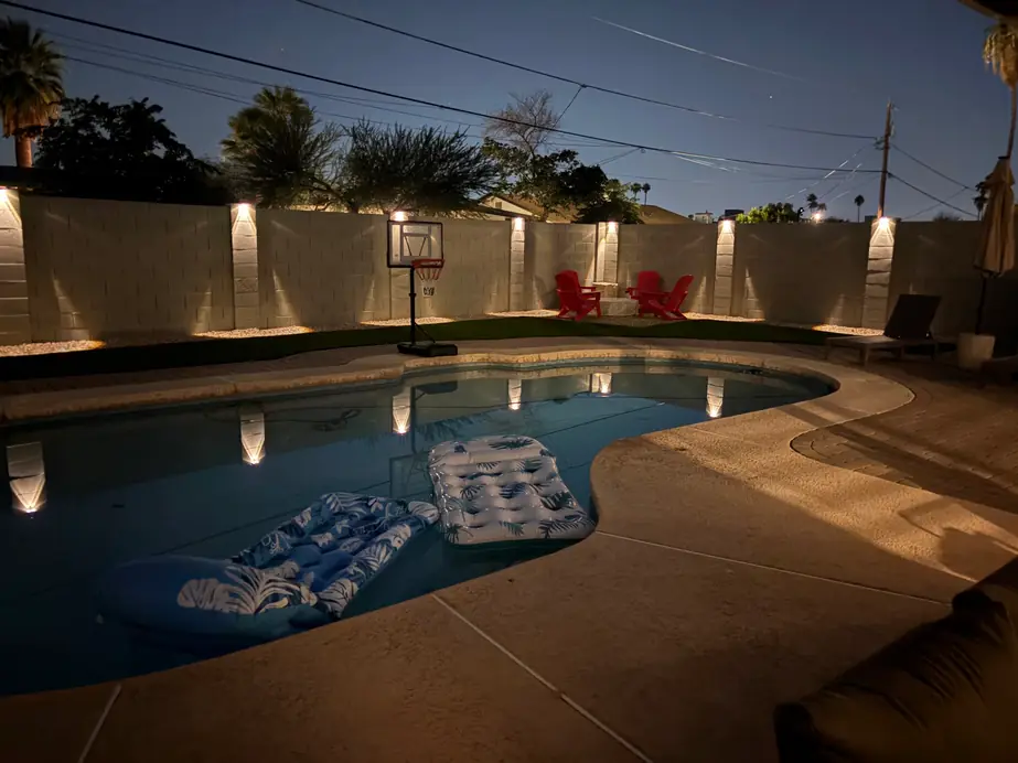 Night pool with lit block wall, uplights and floats on the water